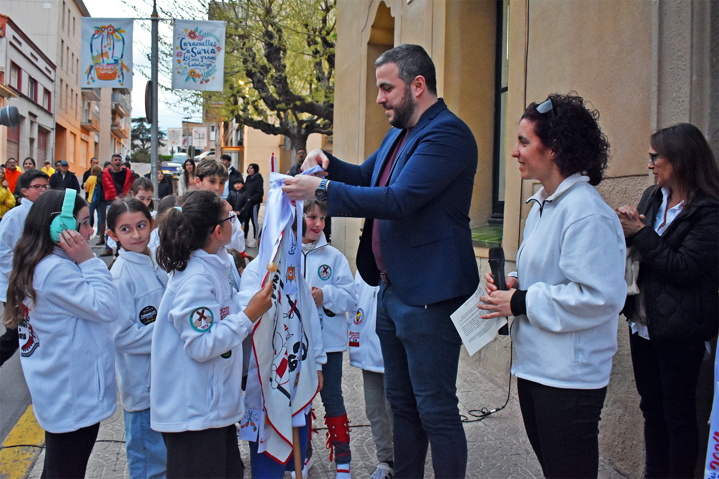 Lliurament de la cinta commemorativa de les Caramelles de SÃºria 2024 a la colla Infantil de lâ€™AgrupaciÃ³ Sardanista, en lâ€™acte dâ€™inici de la festa al davant de la Casa de la Vila.
