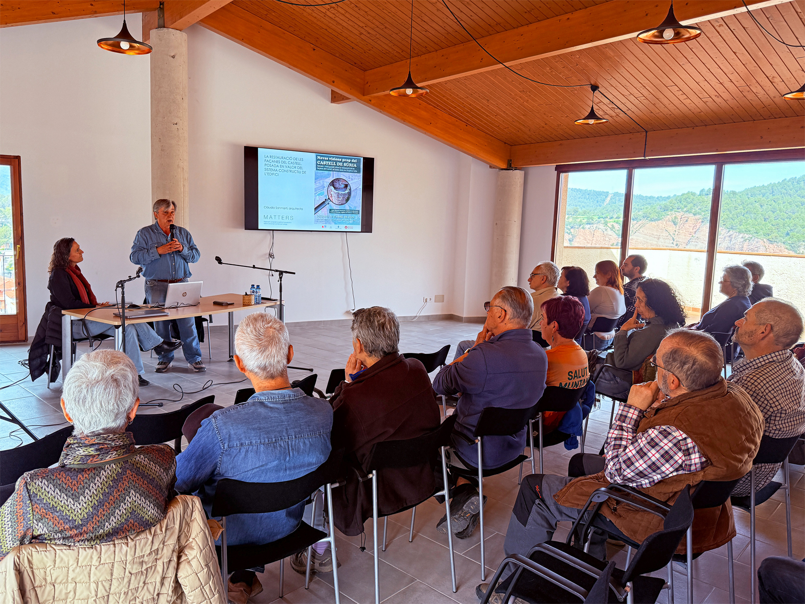 El regidor de Cultura, Albert Fàbrega, parla durant la xerrada 'Noves visions prop del Castell de Súria', a la Sala del Portal de Can Sivila del Lloc (El Casinet), al costat de l'arquitecta Clàudia Sanmartí.
