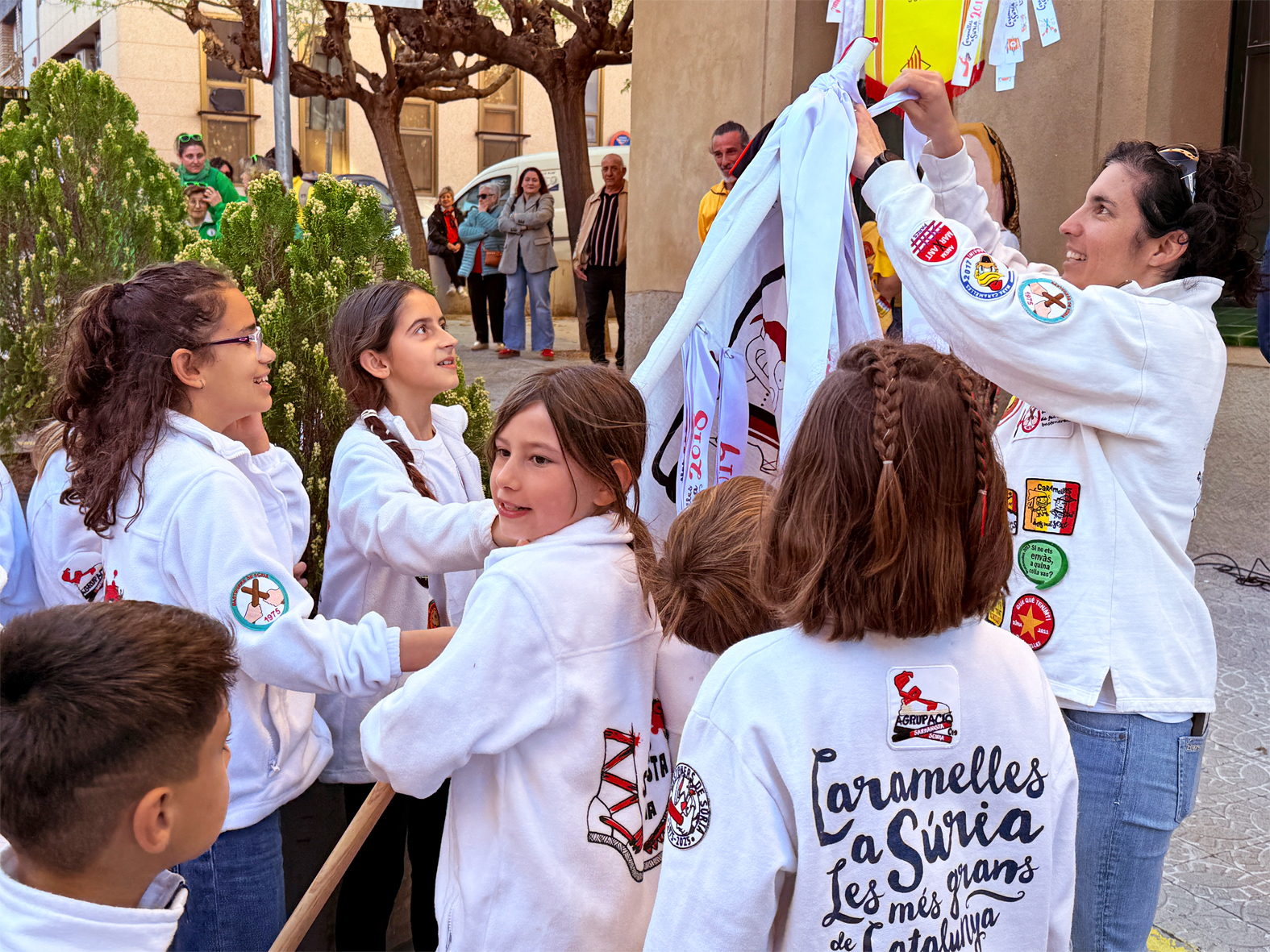 La regidora de Festes, Alba MartÃ­nez, lliura la cinta commemorativa a la colla Infantil de l'AgrupaciÃ³ Sardanista en l'acte d'inici de les Caramelles de SÃºria, al davant de la Casa de la Vila.