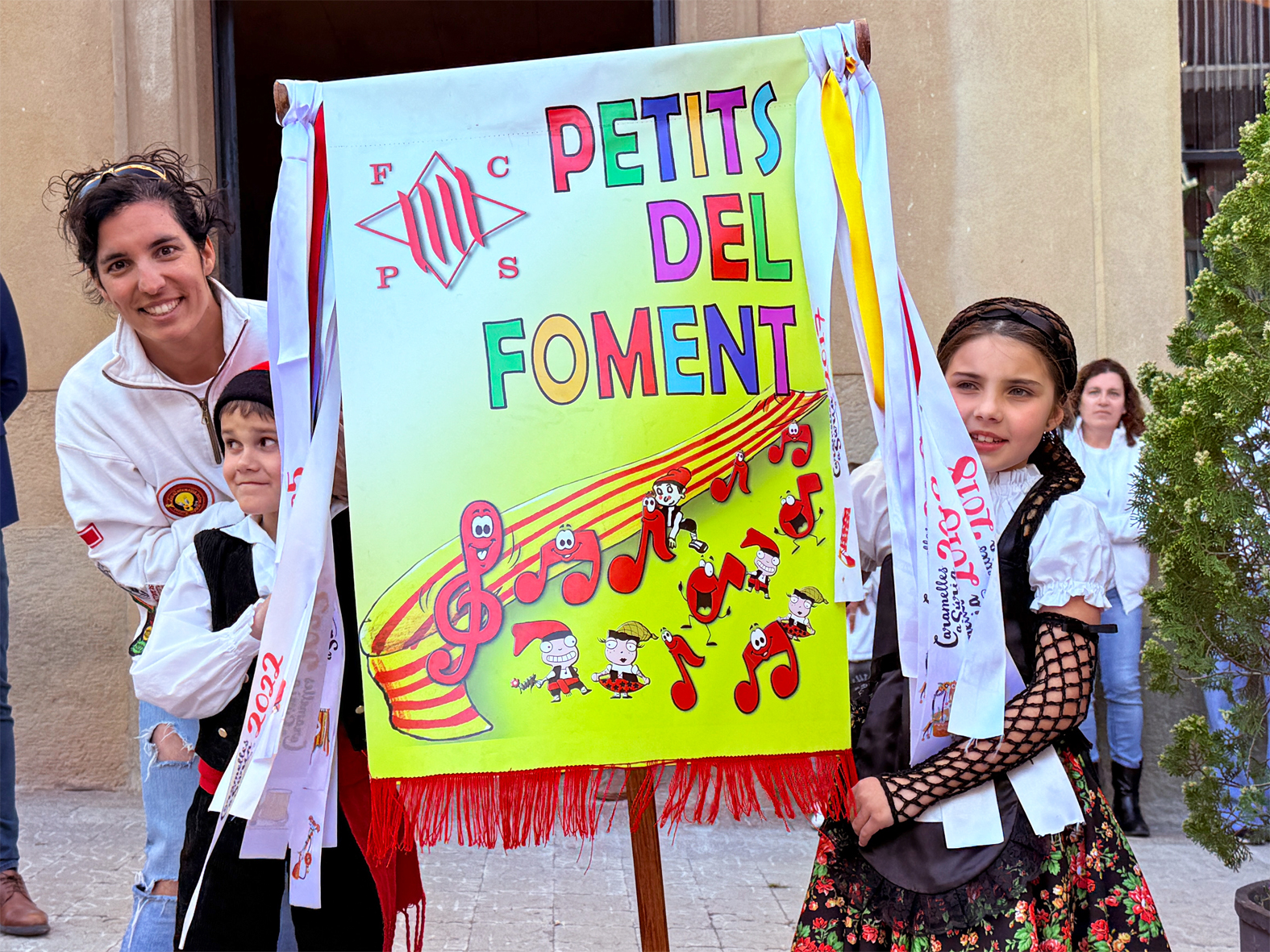 La regidora de Festes, Alba MartÃ­nez, lliura la cinta commemorativa a la colla Infantil del Foment Cultural, en l'acte d'inici de les Caramelles de SÃºria, al davant de la Casa de la Vila.