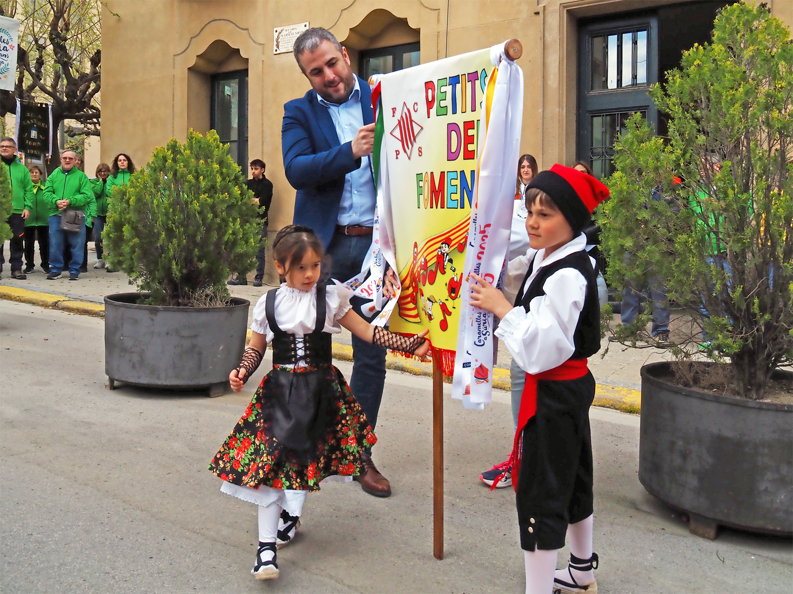 L'alcalde Albert Cober&oacute; lliura la cinta commemorativa a la colla Infantil del Foment Cultural en l'acte d'inici de les Caramelles de S&uacute;ria, al davant de la Casa de la Vila.