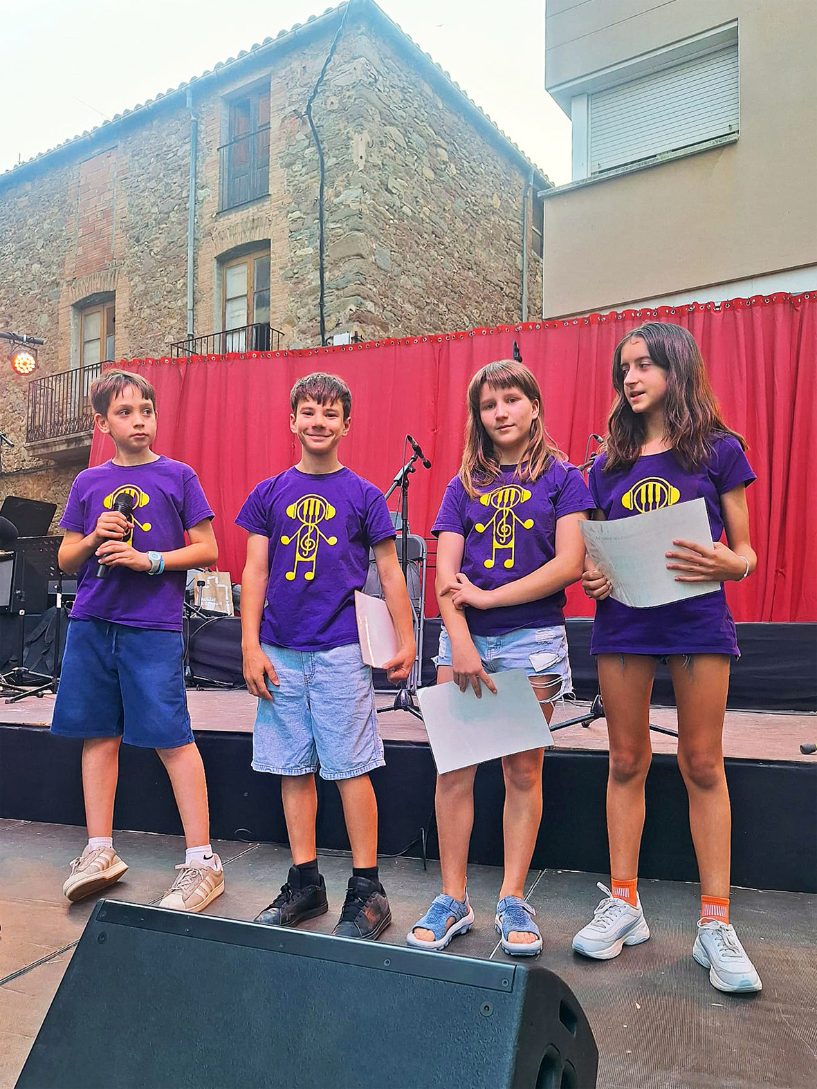 Curs 2025-26 - Representants del Consell Municipal dels Infants anuncien el veredicte del concurs de portades del programa de la Festa Major, durant el Concert d'Estiu de l'Escola Municipal de Musica.