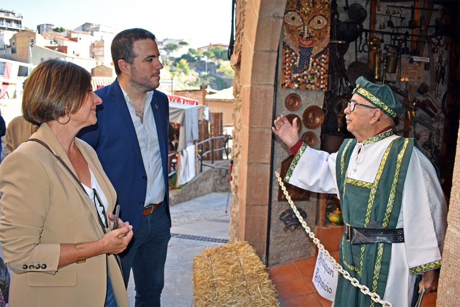 L'alcalde de Súria, Albert Coberó, i la diputada de Turisme de la Diputació de Barcelona, Abigail Garrido, escolten l'antiquari de la 19a Fira Medieval d'Oficis de Súria durant la visita institucional al certamen.