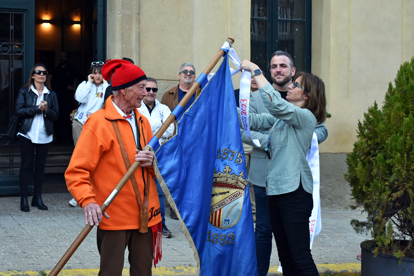 Col·locació de la cinta commemorativa en l'estendard de la Colla del Tro Gros, durant l'acte d'inici de les Caramelles de Súria, al davant de la Casa de la Vila.