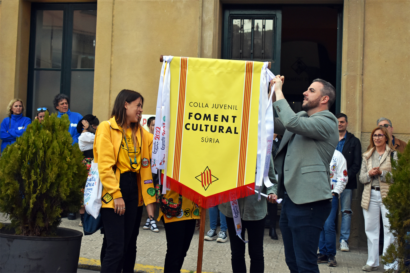 Col·locació de la cinta commemorativa en l'estendard de la Colla Juvenil del Foment Cultural, durant l'acte d'inici de les Caramelles de Súria, al davant de la Casa de la Vila.