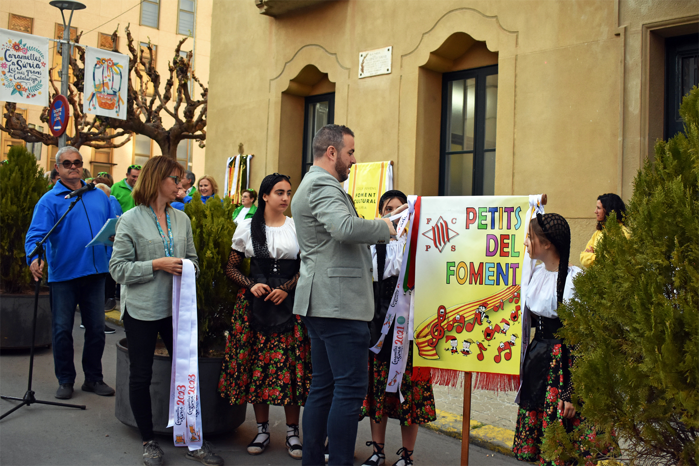 Col·locació de la cinta commemorativa en l'estendard de la Colla Infantil del Foment Cultural, durant l'acte d'inici de les Caramelles de Súria, al davant de la Casa de la Vila.