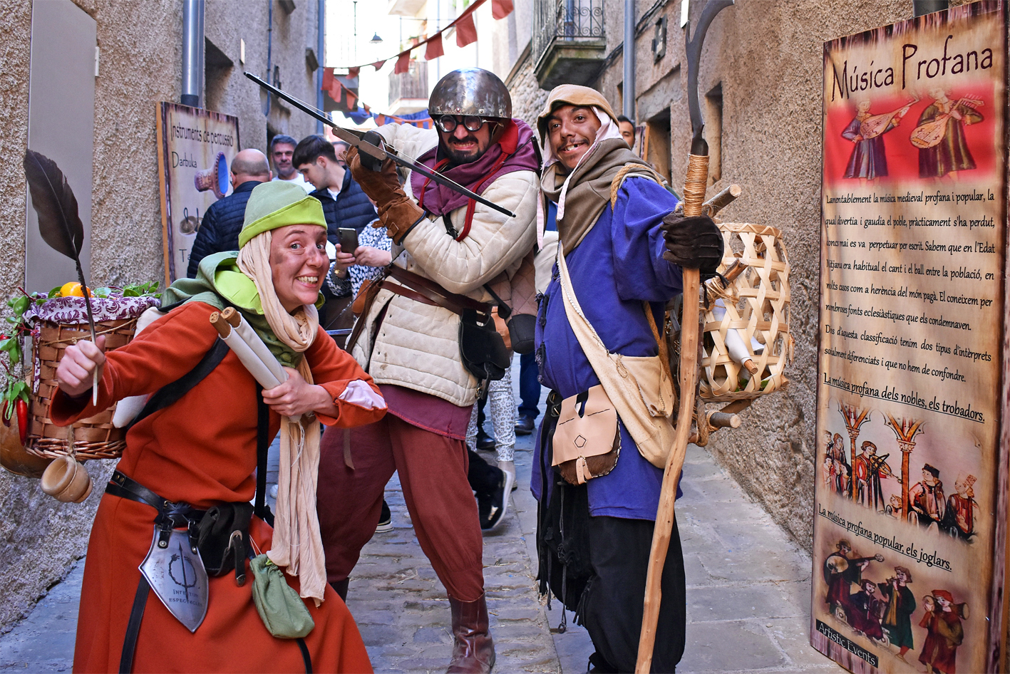 Personatges de la 20a Fira Medieval dâ€™Oficis de SÃºria, al carrer Major, al costat dâ€™un plafÃ³ de lâ€™exposiciÃ³ sobre mÃºsica medieval.